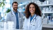 © Pinklife - A male and female doctor are smiling together in a pharmacy, dressed in white coats with medical tools around them, embodying teamwork and positivity.
