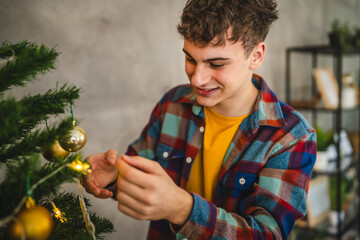 Young man decorate a Christmas tree with festive ornaments at home