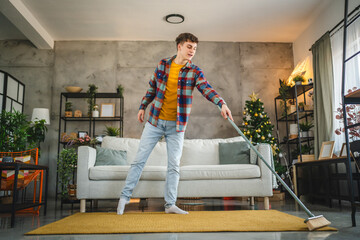 a young adult man do chores stand and clean carpet with a broom