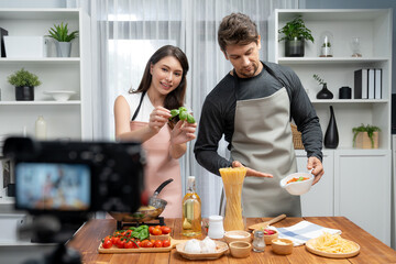 Couple chef influencers on cooking show presenting ingredient of spaghetti, meat, chilli, tomato, garlic and seasoning sauce's homemade special recipe recording on camera on live channel. Postulate.