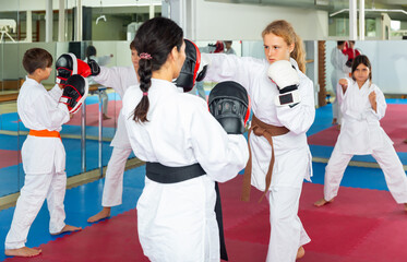 Wall Mural - Female trainer in boxing gloves conducts sparring and teaches punches to a girl in karate and self-defense training