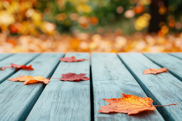 Poster - Dry maple leaves are laying on a blue wooden table with a blurred autumn background