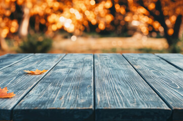 Poster - Empty blue wooden table with fallen autumn leaves in a park, perfect for product placement