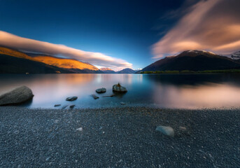 Poster - A serene mountain lake with a rocky shore and a single cloud in the sky.