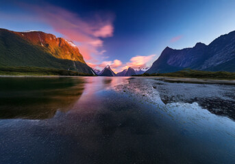 Aufkleber - A calm lake reflects the pink and purple hues of a sunset sky, framed by majestic mountains with snow-capped peaks.