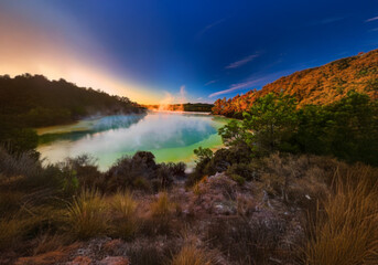 Poster - A green lake surrounded by a lush forest, covered in fog and bathed in the light of dawn.