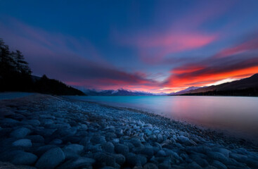 Poster - A tranquil mountain lake with a vibrant red sunset reflecting off the water.