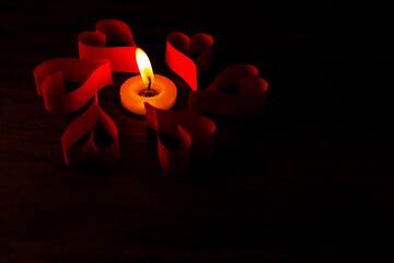 Candle surrounded by red paper hearts on dark background. Space for text. Background, romantic concept, poster, design for your project.