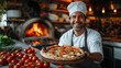 © Алина Бузунова - italian chef smiling and holding pizza with blurred oven with wood burning fire on background .