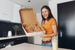 © SHOTPRIME STUDIO - Young woman holding a box of pizza while standing in a modern kitchen interior near the counter