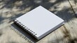 © Aadam - A white square spiral-bound notebook sits on a light-colored wooden surface.