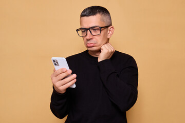 upset man in glasses and jumper looking sad while using his smartphone to read messages and connect 