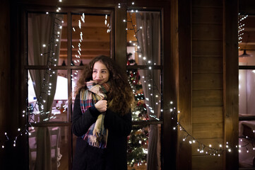 Student is coming home from university for the Christmas holidays, standing in front of house window, living room with christmas tree behind her.