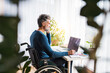 © Halfpoint - Handsome man in wheelchair working from home office, making phone call and writing notes in planner. Telecommuting and home office.