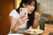 © Prathankarnpap - Portrait of a beautiful asian woman having breakfast and using smartphone at kitchen table