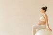© NN AI - Portrait of a caucasian pregnant woman doing exercises in beige activewear on a fitness ball isolated on a beige background. fitness, pregnancy concept. Banner, poster, wallpaper, copy space