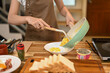 © Prathankarnpap - Young woman in brown apron serving scrambled eggs from a pan onto a white plate