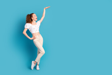 Poster - Full size photo of pretty young girl show high measure empty space wear trendy white outfit isolated on blue color background