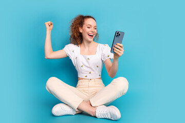 Wall Mural - Full size photo of pretty young girl sit floor hold device winning excited wear trendy white outfit isolated on blue color background