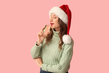 Wall Mural - Young woman in Santa hat with glass of champagne on pink background