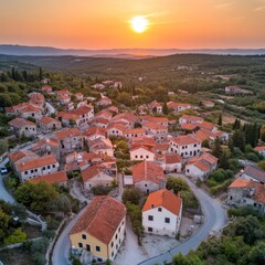 Aerial view of a charming village at sunset with terracotta-roofed houses surrounded by lush greenery.