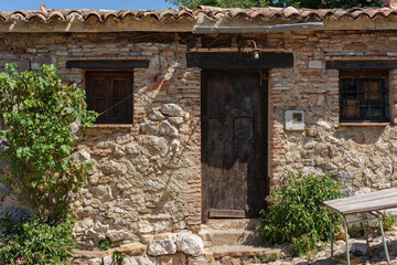 facade of an old house made of bricks and stones, with doors and windows of old wood and worn tiles, decorated with some green plants.