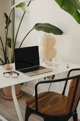 Wall Mural - elegant white desk with laptop, glasses, and unique lamp surrounded by vibrant green plants for offi