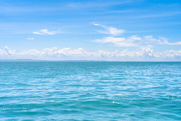 Serene sea ocean view with gentle waves, distant mountains, and a blue sky with clouds.