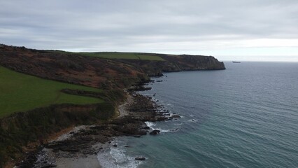 Scenic rocky coastline with green fields and a ship on the horizon.