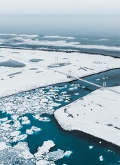 Aerial view of snowy landscape with bridge over icy river and ocean.