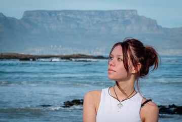 Young woman in a white top and black pants sitting on a boulder next to the ocean