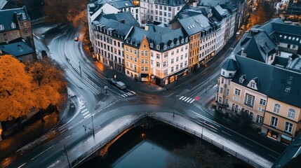 Aerial view of a European cityscape with historic buildings, streets, and cars at dusk with autumn trees and wet roads, featuring a central illuminated intersection.