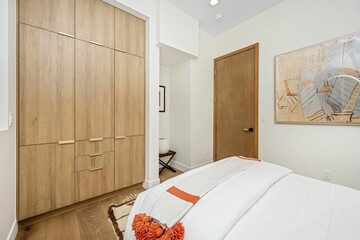 Modern bedroom with wooden wardrobe, abstract art, and cozy bedding in neutral tones