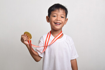 Little Asian boy smiling happily holding a gold medal on his chest isolated on a white background. The boy celebrating his victory