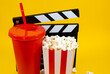 © Answer 7 - Horizontal image of popcorn with a red soda glass and a white and black wooden clapperboard and scattered popcorn on a yellow background, concept of cinema food and entertainment