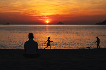 Silhouettes of people relaxing on the beach by the sea in the evening at sunset in summer on vacation