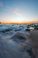 Wall Mural - peaceful sunrise over a rocky beach shore.