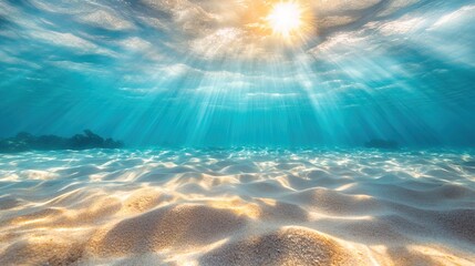 Underwater view of the clear, sandy ocean floor with sunlight 