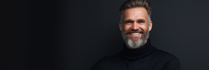 A man with a beard and gray hair is smiling and wearing a black sweater. He looks happy and content