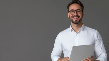 Poster - Young man with glasses stands confidently holding a laptop in a modern office setting during the day