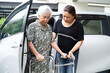 © manassanant - Caregiver help Asian elderly woman disability patient get in her car.