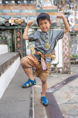 Wall Mural - Little asian boy wear traditional local Thai man suit travel in buddhist temple of dawn