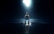 © YiuCheung - A glass bottle of perfume stands alone on a dark, wet surface with a spotlight overhead.