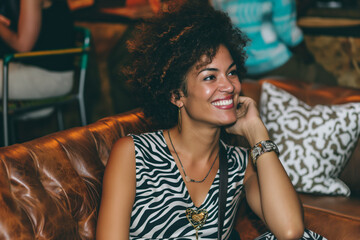 Black woman model sitting brown leather couch at a trendy nightclub wearing a leopard print dress. African american lady relaxing on a sofa party. Nighttime setting with a candid photography style