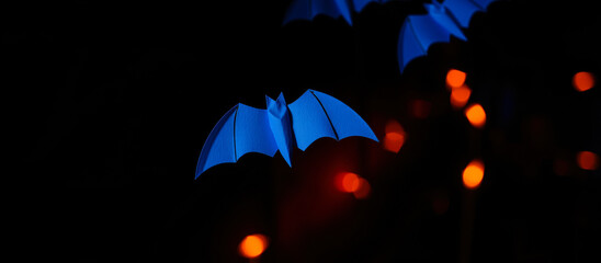 Canvas Print - blue paper bat hangs against a blurred background lights