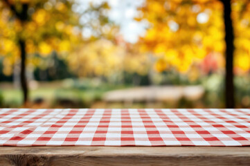 Aufkleber - Red and white checkered tablecloth on a wooden picnic table with blurred autumn foliage in the background. Outdoor dining and fall season concept