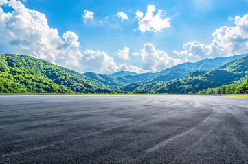 Empty asphalt road leading to green mountain under blue sky