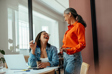 Happy women laughing and collaborating in a colorful modern office with coffee