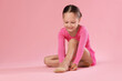 © New Africa - Little ballerina putting on pointe shoes against pink background, space for text