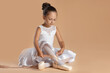 © New Africa - Little ballerina tying pointe shoes on beige background